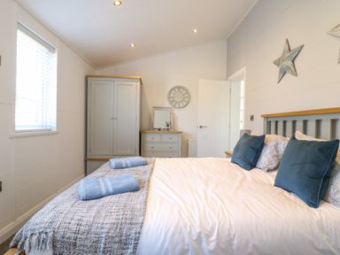 A bedroom with a bed with blue pillows and towels a wardrobe a chest of drawers and a clock on the wall at Number 43 The Poplars in Burnham Market
