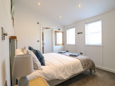 A bedroom with a bed with pillows and folded towels near two windows and a bedside lamp at Number 43 The Poplars Burnham Market