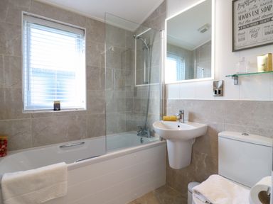 A bathroom with bathtub shower white sink toilet and a window with blinds at Number 43 The Poplars in Burnham Market