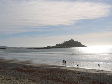 A beach scene with people walking by the water at Kittiwake in Newlyn