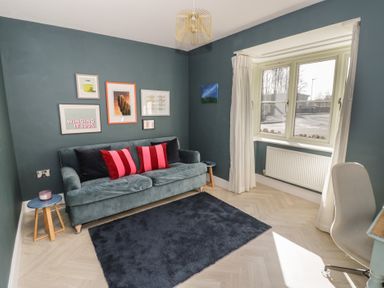 A living room with a green sofa red and black cushions a blue rug and framed pictures on the wall at 2 Summers Way in Moreton-In-Marsh