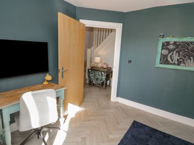 A room with a wooden desk chair tv mounted on wall and open door showing a hallway at 2 Summers Way in Moreton-In-Marsh