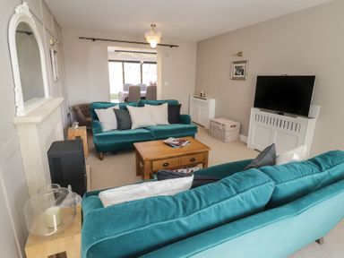 A living room with teal sofas a wooden coffee table a television on a white stand and a fireplace at 2 Summers Way in Moreton-In-Marsh