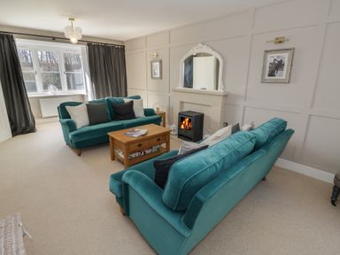 A living room with teal sofas a wooden coffee table and a fireplace at 2 Summers Way in Moreton-In-Marsh