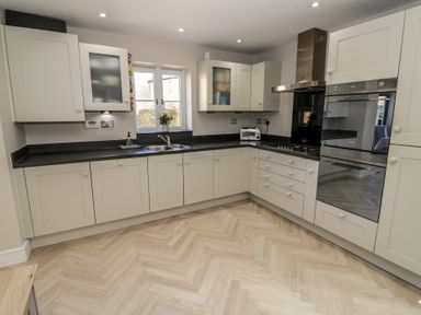 A modern kitchen with white cabinets black countertops a double sink a window a stainless steel oven and a gas stove at 2 Summers Way in Moreton-In-Marsh