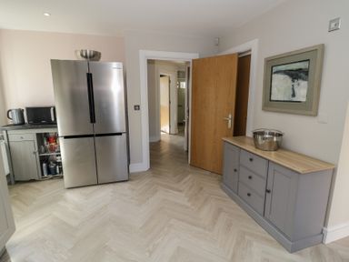 A kitchen with a stainless steel refrigerator a grey cabinet with drawers and doors a microwave a kettle and an open wooden door at 2 Summers Way in Moreton-In-Marsh