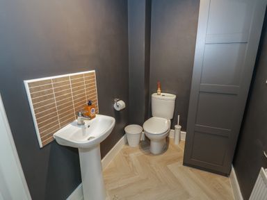 A bathroom with a white sink, toilet, storage cabinet, and gray walls at 2 Summers Way in Moreton-In-Marsh