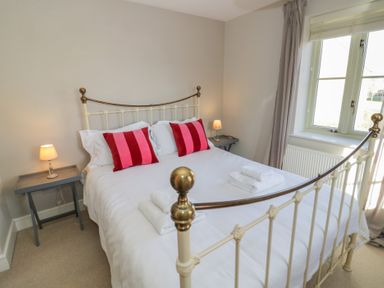 A bedroom with a metal bedframe two bedside tables with lamps and windows with curtains at 2 Summers Way in Moreton-In-Marsh