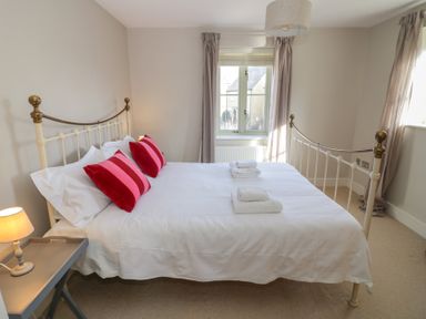 A bedroom with a metal bed frame with white bedding and red pillows at 2 Summers Way in Moreton-In-Marsh