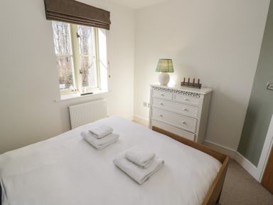 A bedroom with a bed with folded towels next to a chest of drawers with a lamp at 2 Summers Way in Moreton-In-Marsh