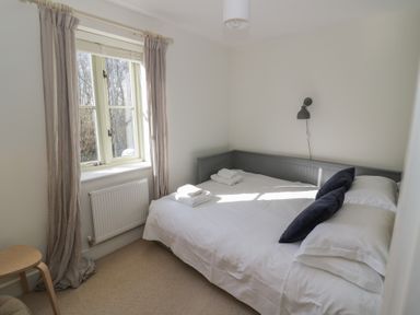 A small bedroom with a bed against the wall a window with curtains and a radiator at 2 Summers Way in Moreton-In-Marsh