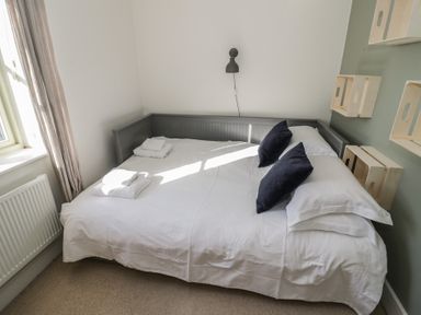 A bedroom with a bed with white bedding two black pillows and wooden shelves on the wall at 2 Summers Way in Moreton-In-Marsh