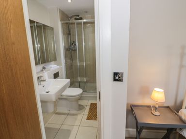 A bathroom with a sink toilet and glass shower next to a bedside table with a lamp at 2 Summers Way in Moreton-In-Marsh