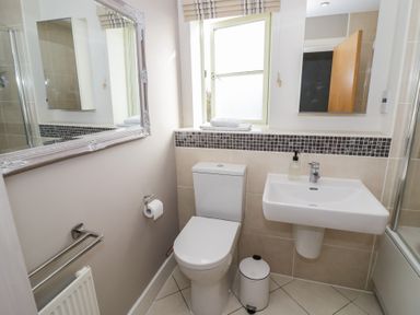 A bathroom with a toilet a sink a waste bin a towel rack and a window at 2 Summers Way in Moreton-In-Marsh