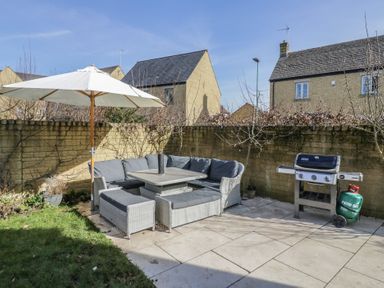 An outdoor patio area with a sectional sofa under a white umbrella and a barbecue grill at 2 Summers Way in Moreton-In-Marsh