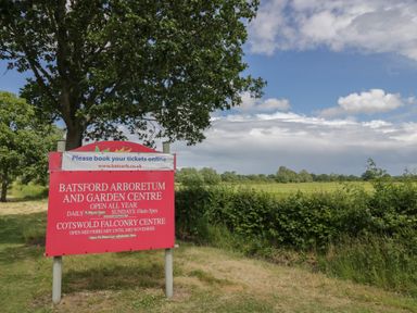 A sign for Batsford Arboretum and Garden Centre in a grassy area with trees and a partly cloudy sky