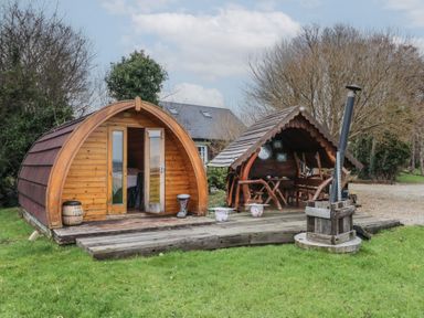 A wooden pod and covered seating area on a wooden deck with grass and trees at River View Pod near Muff County Donegal