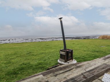 A grassy yard with a wood-burning stove on a wooden deck overlooking a tidal flat at River View Pod near Muff County Donegal