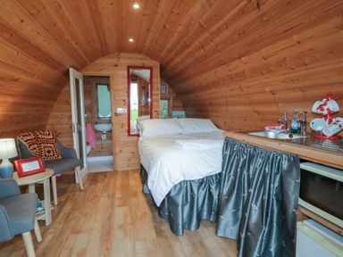 A wooden pod interior with a bed a small kitchenette two chairs a small table and a bathroom at River View Pod near Muff County Donegal