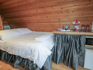 A bedroom with a white bed next to a small kitchen sink area with teacups and containers at River View Pod near Muff County Donegal