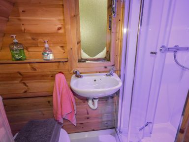 A bathroom with a sink a towel a shower and wooden walls at River View Pod near Muff County Donegal