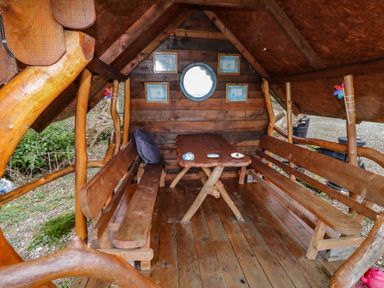 A small wooden cabin interior with a table and benches and framed pictures on the wall at River View Pod near Muff County Donegal