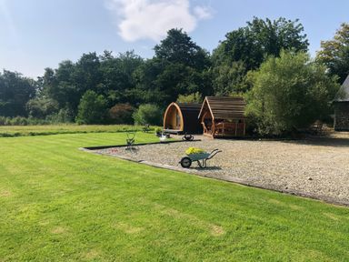 A grassy yard with a small wooden pod and a covered wooden seating area near trees at River View Pod near Muff County Donegal