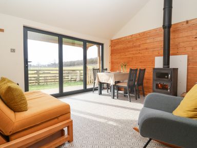 A dining area with table and chairs next to a wood stove and large sliding glass doors at Beech Tree Cabin in Goodmanham near Market Weighton