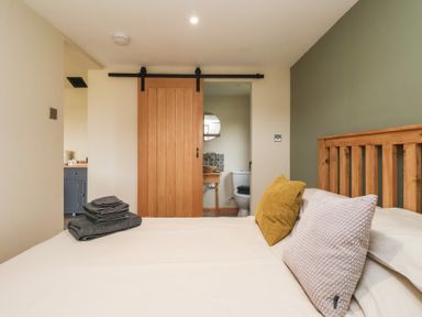 A bedroom with a bed with pillows and folded towels near a wooden sliding door opening to a bathroom at Beech Tree Cabin in Goodmanham near Market Weighton