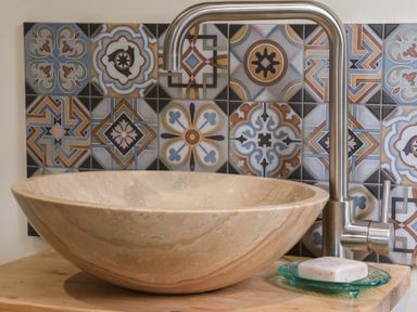 A stone sink with a silver faucet and soap on a green dish in front of decorative patterned tiles at Beech Tree Cabin in Goodmanham near Market Weighton