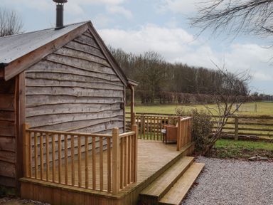 A wooden cabin with a deck and railing in a rural setting at Beech Tree Cabin in Goodmanham near Market Weighton