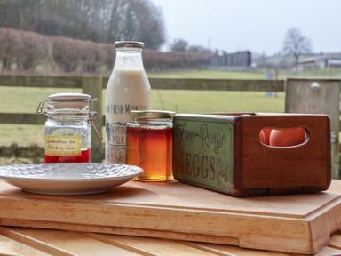 A jar of jam a bottle of milk a jar of honey and a box of free range eggs on wooden boards with a countryside view at Beech Tree Cabin in Goodmanham near Market Weighton