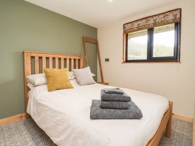 A bedroom with a wooden bed frame a window with floral curtain and towels on the bed at Beech Tree Cabin in Goodmanham near Market Weighton