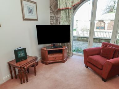A corner of a room with a television on a wooden stand a red armchair and nested wooden tables at Aubretia Trail in Akeld near Wooler