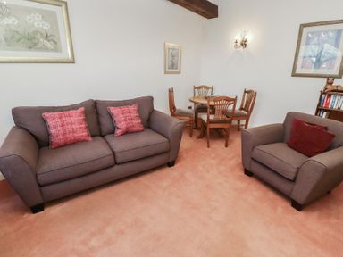 A living room with a sofa and armchair with red cushions and a wooden dining table with chairs at Aubretia Trail in Akeld near Wooler