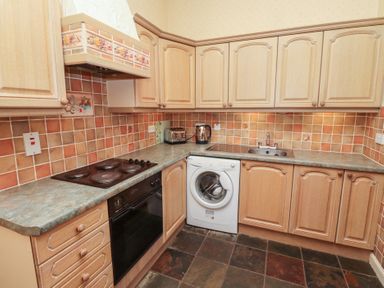 A kitchen with wooden cabinets a washing machine an oven stove kettle and toaster at Aubretia Trail in Akeld near Wooler