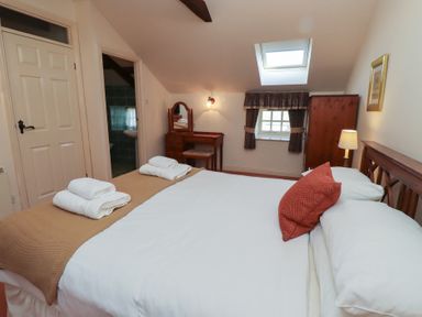 A bedroom with a double bed white linens and red pillows a wooden dressing table and a wardrobe at Aubretia Trail in Akeld near Wooler