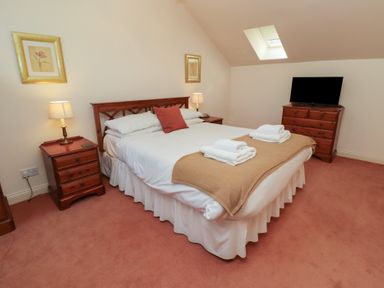 A bedroom with a double bed towels on blanket bedside tables lamps a dresser with television and skylight at Aubretia Trail in Akeld near Wooler
