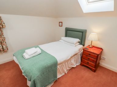 A single bed with green headboard and blanket next to a wooden nightstand with a lamp at Aubretia Trail Akeld near Wooler