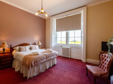 A bedroom with a bed, nightstand, lamp, and windows at Cheviot Manor near Wooler