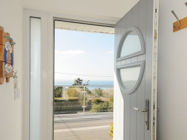 An open door leading to a balcony with glass railing and a view of trees and the sea at Atlanta near Tintagel