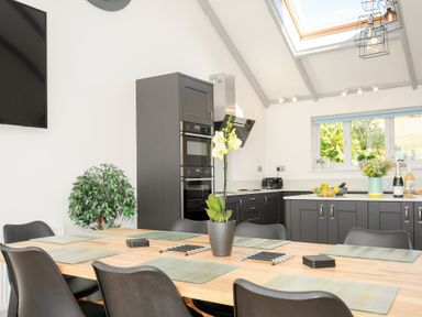 A kitchen with a wooden dining table and black chairs with placemats and a plant in a pot at Atlanta near Tintagel