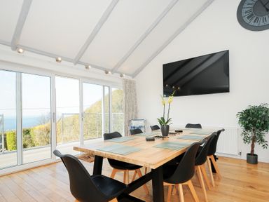 A dining room with a wooden table and black chairs next to large sliding glass doors and a wall-mounted TV at Atlanta near Tintagel