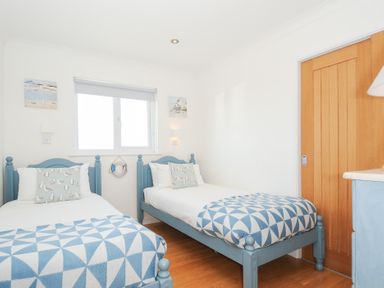 A bedroom with two single blue beds with white and blue bedding a wooden door and a window at Atlanta near Tintagel