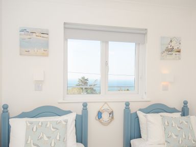 A bedroom with two blue beds and seagull pillows under a window with ocean view at Atlanta near Tintagel