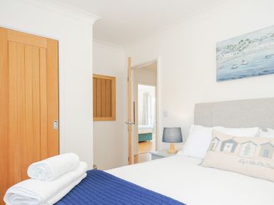 A bedroom with a bed white linens blue blanket pillows wooden door and a bedside table with a lamp at Atlanta near Tintagel