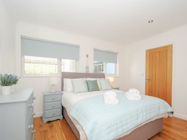 A bedroom with a bed covered in light blue bedding two rolled white towels on top light blue nightstands with lamps a light blue chest of drawers with a potted plant wooden floor and a wooden door at Atlanta near Tintagel