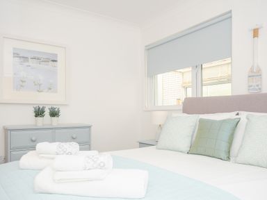 A bedroom with a bed with pillows and folded towels on it a dresser with two potted plants and a framed painting on the wall at Atlanta near Tintagel