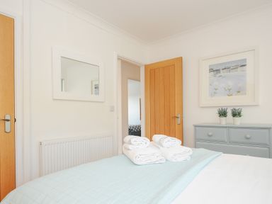 A bedroom with a bed covered with a light blue and white quilt four folded white towels on the bed a light blue dresser with two potted plants and a framed picture on the wall at Atlanta near Tintagel