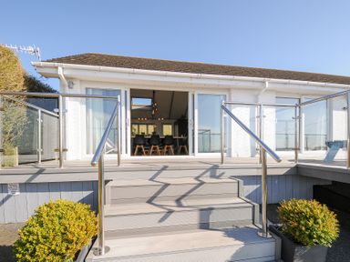 A deck with stairs and glass railings leading to a room with a dining table and chairs at Atlanta near Tintagel